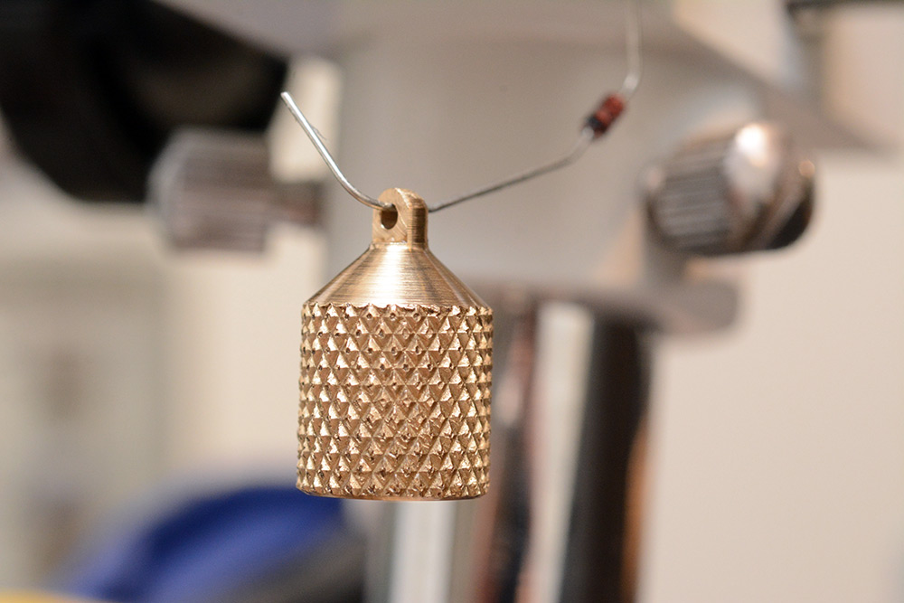 Knurled brass earring drying, supported by the bent leg of a diode