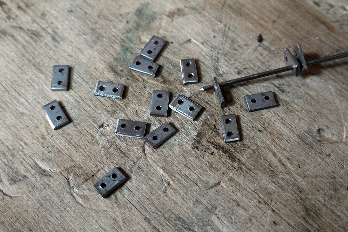 Sixteen hinge links partially finished, three threaded onto a 1.6mm filled rod