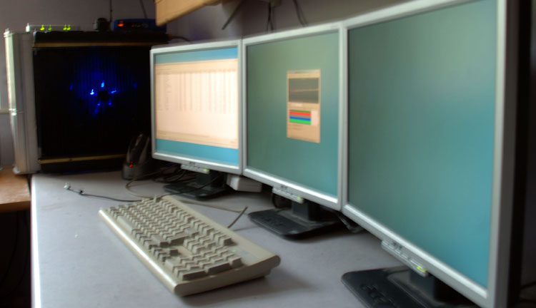 The finished PC, with blue glow through the radiator and three monitors on the desk